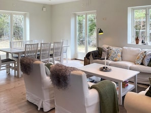 Un salon moderne avec un coin repas, des meubles blancs et de grandes fenêtres.