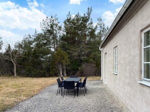 An outdoor patio with a table and chairs, surrounded by a gravel area and trees.