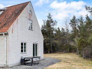 A single-story building with a sloped roof, a gravel driveway, and a table with chairs outside.