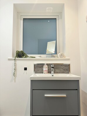 A bathroom with a window, a mirror, a sink, and a cabinet. - Eagle Cottage, 3 - Bed - Long Term Rental Available (Ulverston)