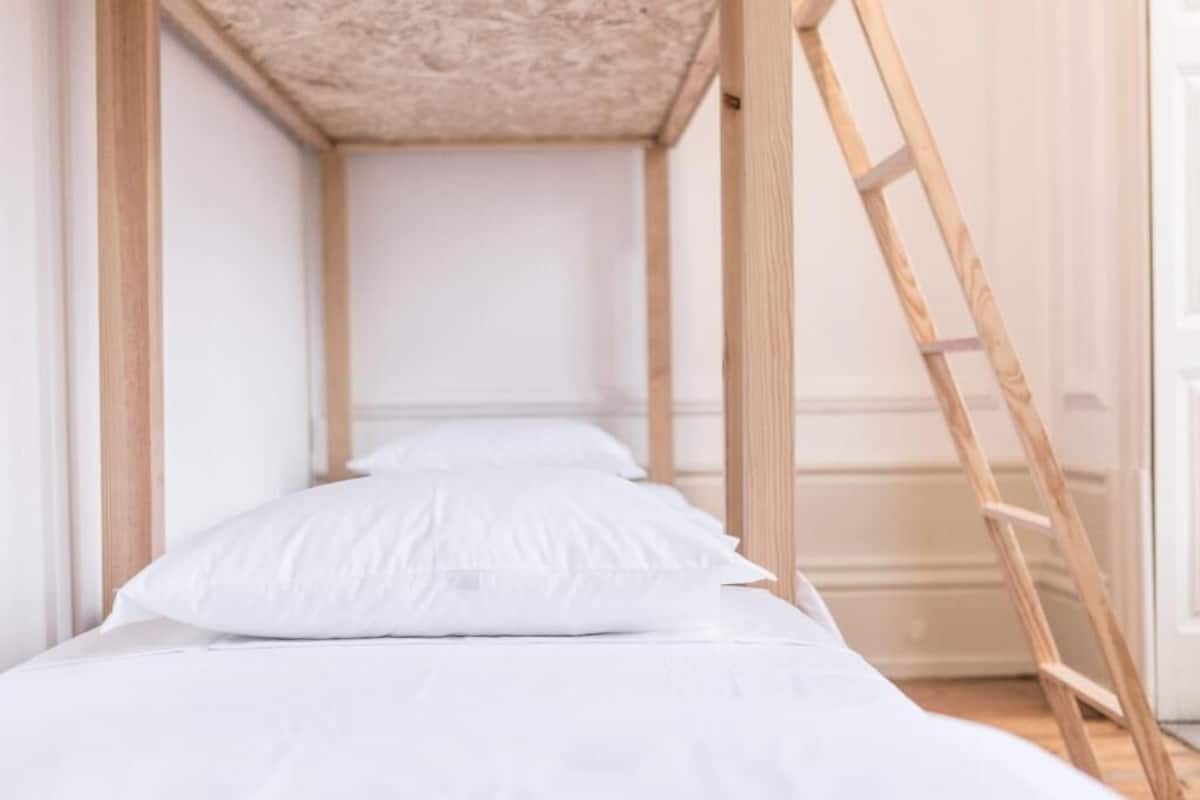 A bunk bed with white bedding and a wooden ladder.