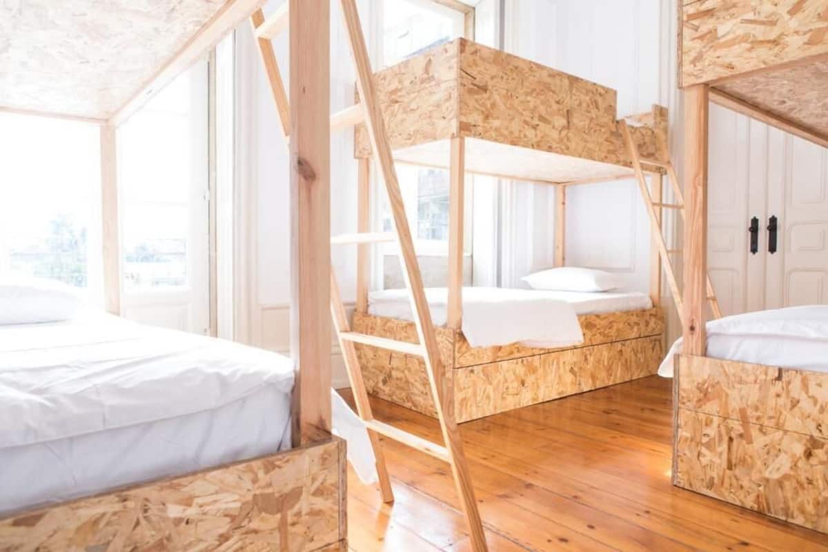 A room with bunk beds made of wood, wooden floors, and white bedding.