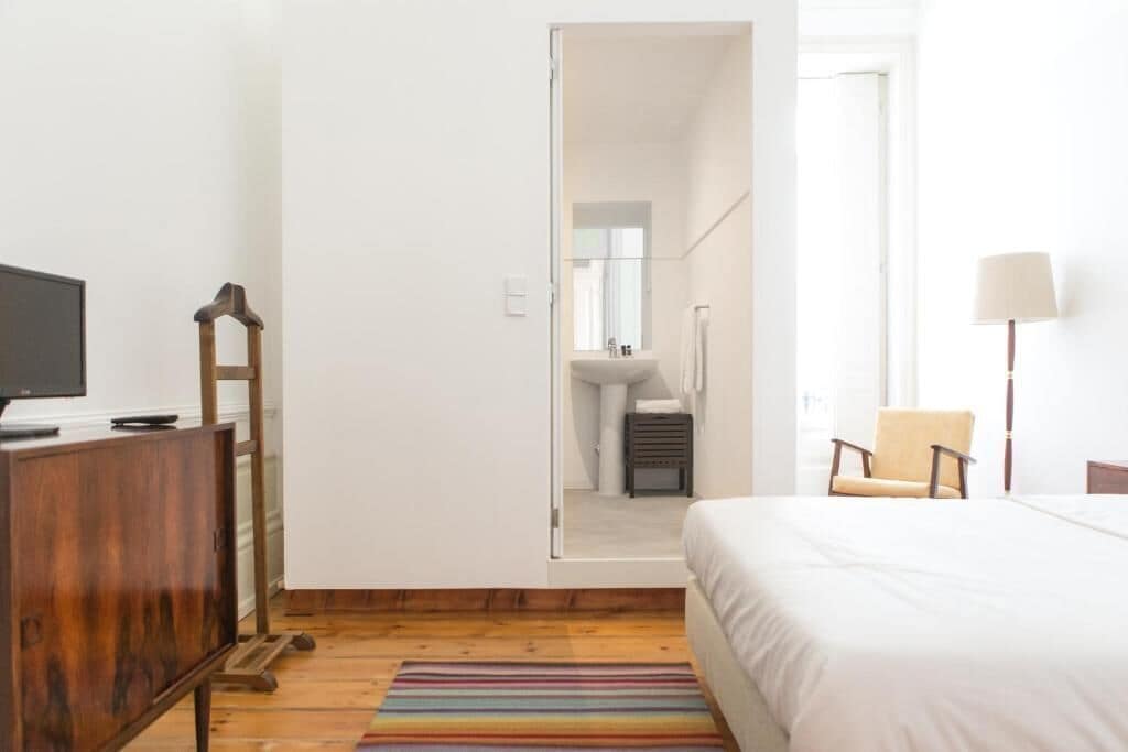 Un dormitorio con una cama, un aparador de madera, una silla, una lámpara y vistas al baño.