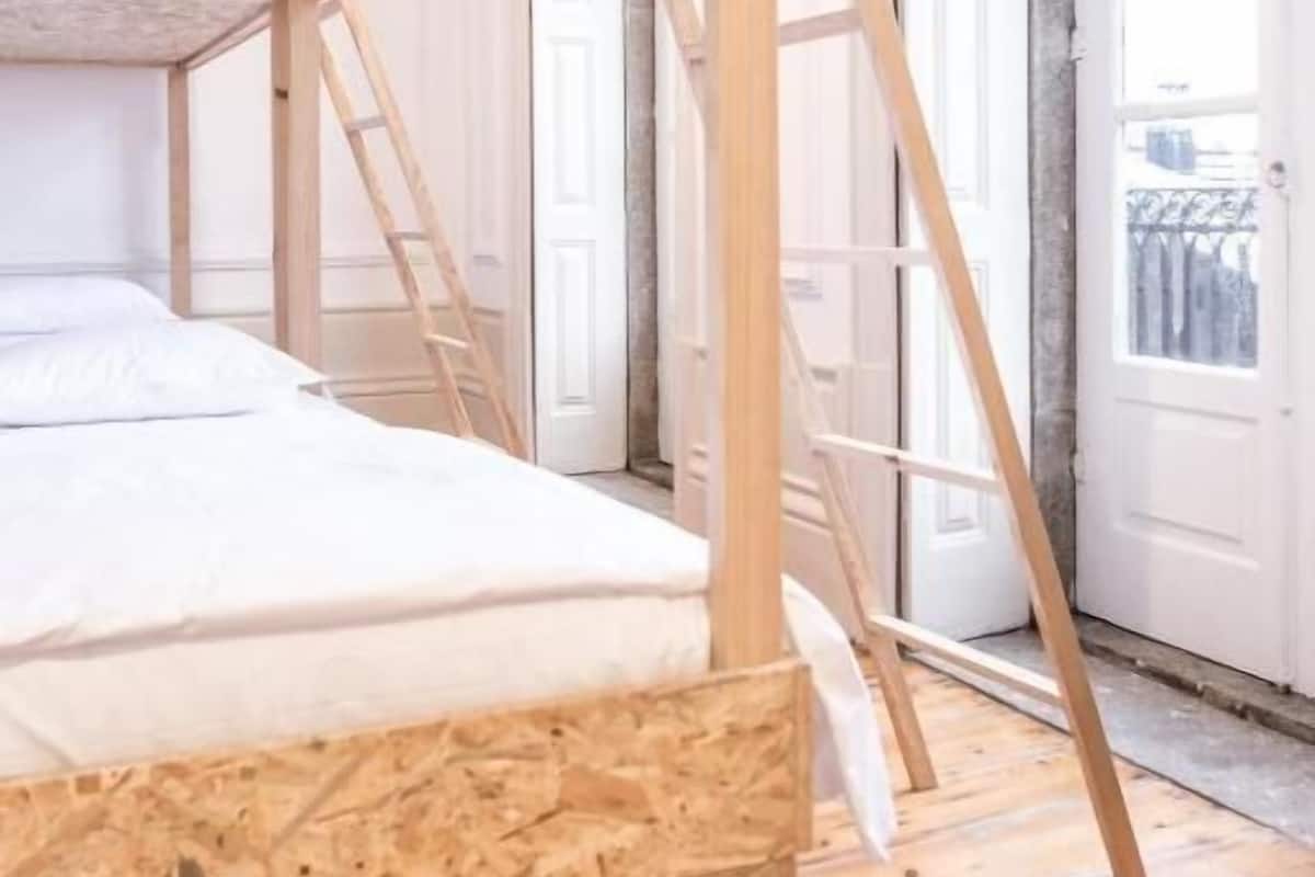 A bunk bed with a wooden frame and a ladder, a white mattress, and a wooden floor.