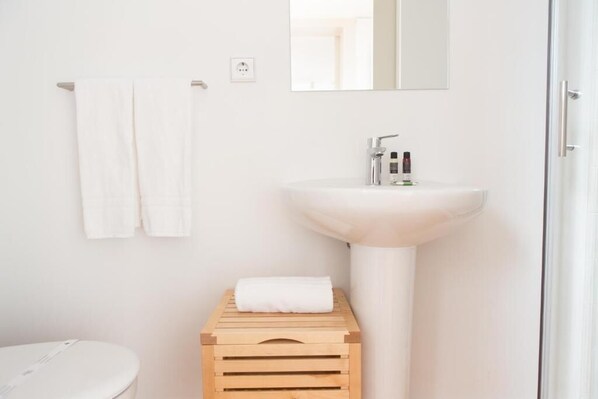 Un bagno dal design minimalista con un lavandino bianco, uno specchio e due asciugamani bianchi appesi al muro.