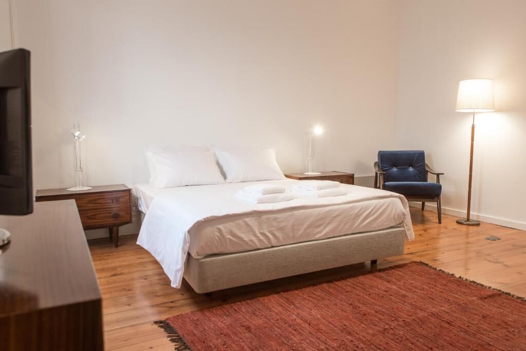 Um quarto bem arrumado com cama, mesas de cabeceira, uma cadeira e abajur.