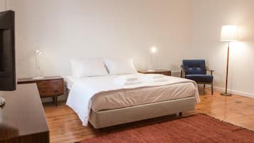 Um quarto bem arrumado com cama, mesas de cabeceira, uma cadeira e abajur.