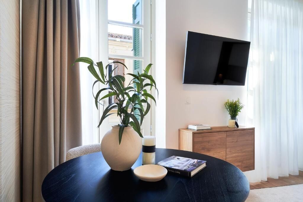 Una sala de estar moderna con una mesa redonda, una planta en maceta, un libro, una vela y un televisor en la pared.