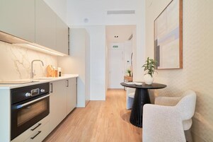 Una cocina moderna con armarios blancos, encimera de mármol y estufa negra. Hay un comedor con una mesa redonda y dos sillas.