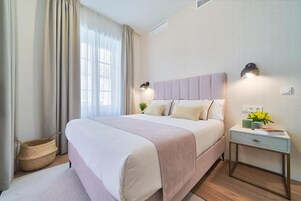 Un dormitorio con cama, mesitas de noche, lámpara y ventana con cortinas.