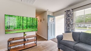 A living room with a large flat-screen TV, a gray sofa, and a wooden entertainment unit. - Ocean Breeze Escape! (Ocean Isle Beach)