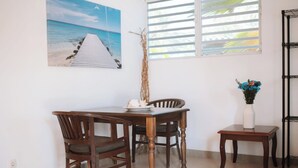 Ein Essbereich mit Holztisch und Stühlen, einem kleinen Beistelltisch mit einer Vase sowie einem Strandbild an der Wand.
