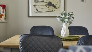 Un comedor con una mesa de madera, sillas tapizadas en negro y un florero blanco con follaje verde.