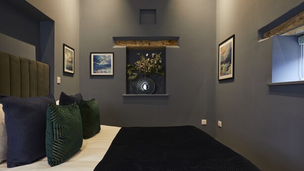 Un dormitorio moderno con una cama grande, paredes oscuras y obras de arte enmarcadas.