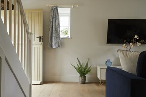A room with a staircase, a window with a curtain, a potted plant, a side table with a vase, and a sofa. - A charming blend of modern comfort and rustic charm, Wisteria is a stylish retreat—perfect for coupl (Cirencester)