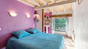 Ein Schlafzimmer mit Bett, Fenster, Waschbecken und Blick ins Grüne.