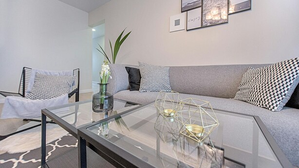 A modern living room with a glass coffee table, grey sofa, patterned cushions, and framed artwork on the wall. - Super apartment (Mérignac)