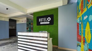 A hotel reception desk with a 'HOTELO' sign, a green wall, and a colorful mural.