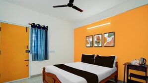 A hotel room with a bed, a ceiling fan, a window with curtains, and artwork on the wall.