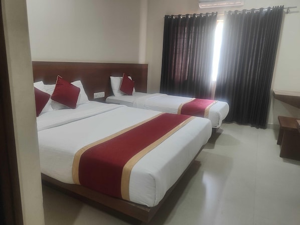 Habitación de hotel con dos camas, cada una con ropa blanca y detalles rojos, un cabecero de madera y una ventana con cortinas oscuras.