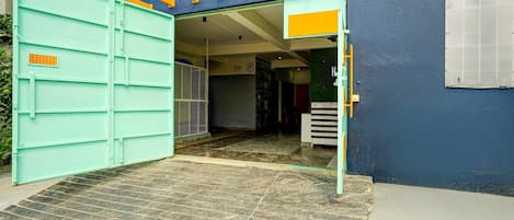 Una entrada abierta a un edificio con una reja verde, piso de baldosas y pasamanos amarillo.