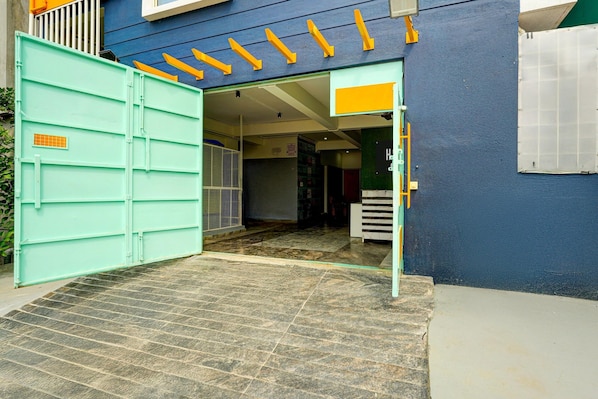 Una entrada abierta a un edificio con una reja verde, piso de baldosas y pasamanos amarillo.