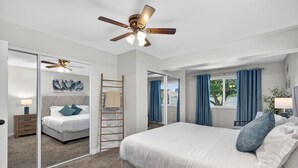 Ein modernes Schlafzimmer mit einem großen Bett, einem Deckenventilator, einer Himmelsleiter und Blick ins Freie durch ein Fenster.