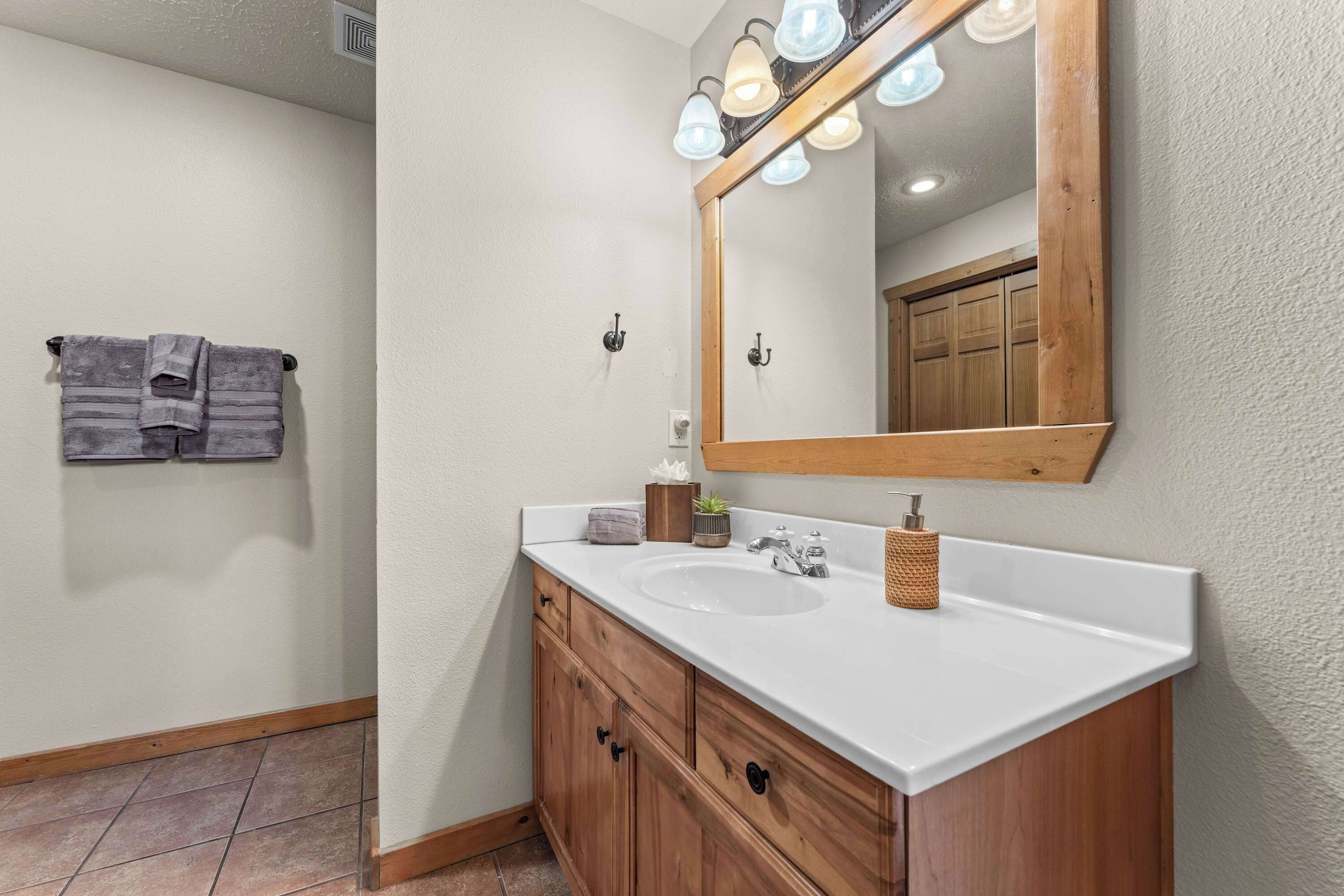 A bathroom with a white sink, wooden vanity, and a mirror with lights.