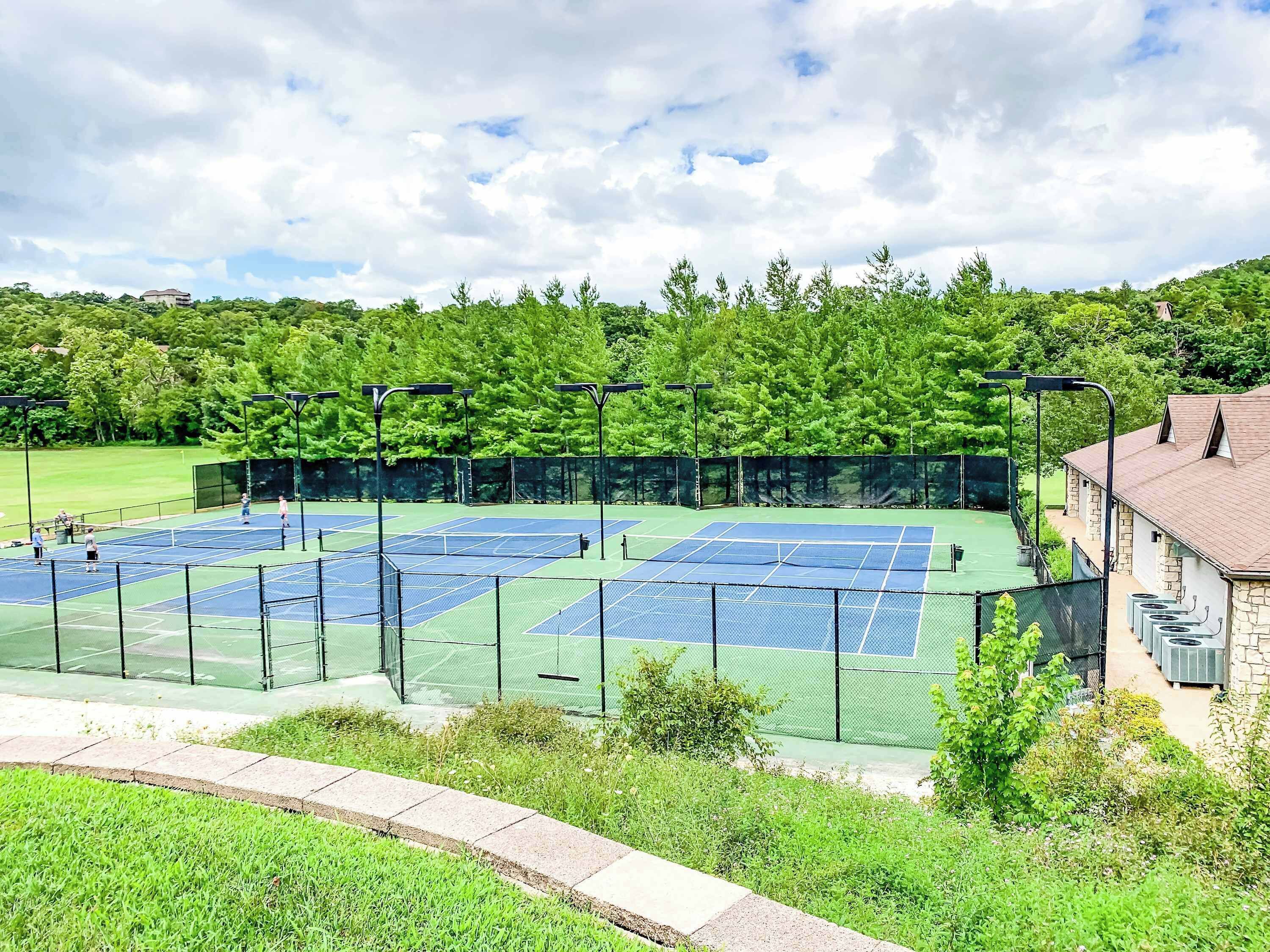 Un court de tennis entouré d’une clôture, avec des arbres en arrière-plan.