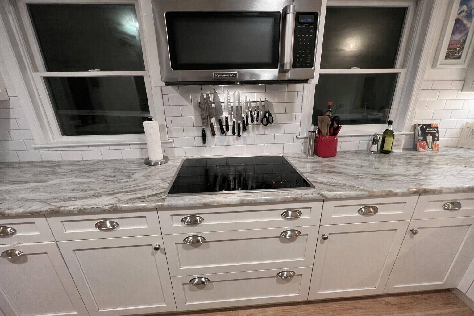 A kitchen with white cabinets, a black stove, a microwave, and a window with blinds.