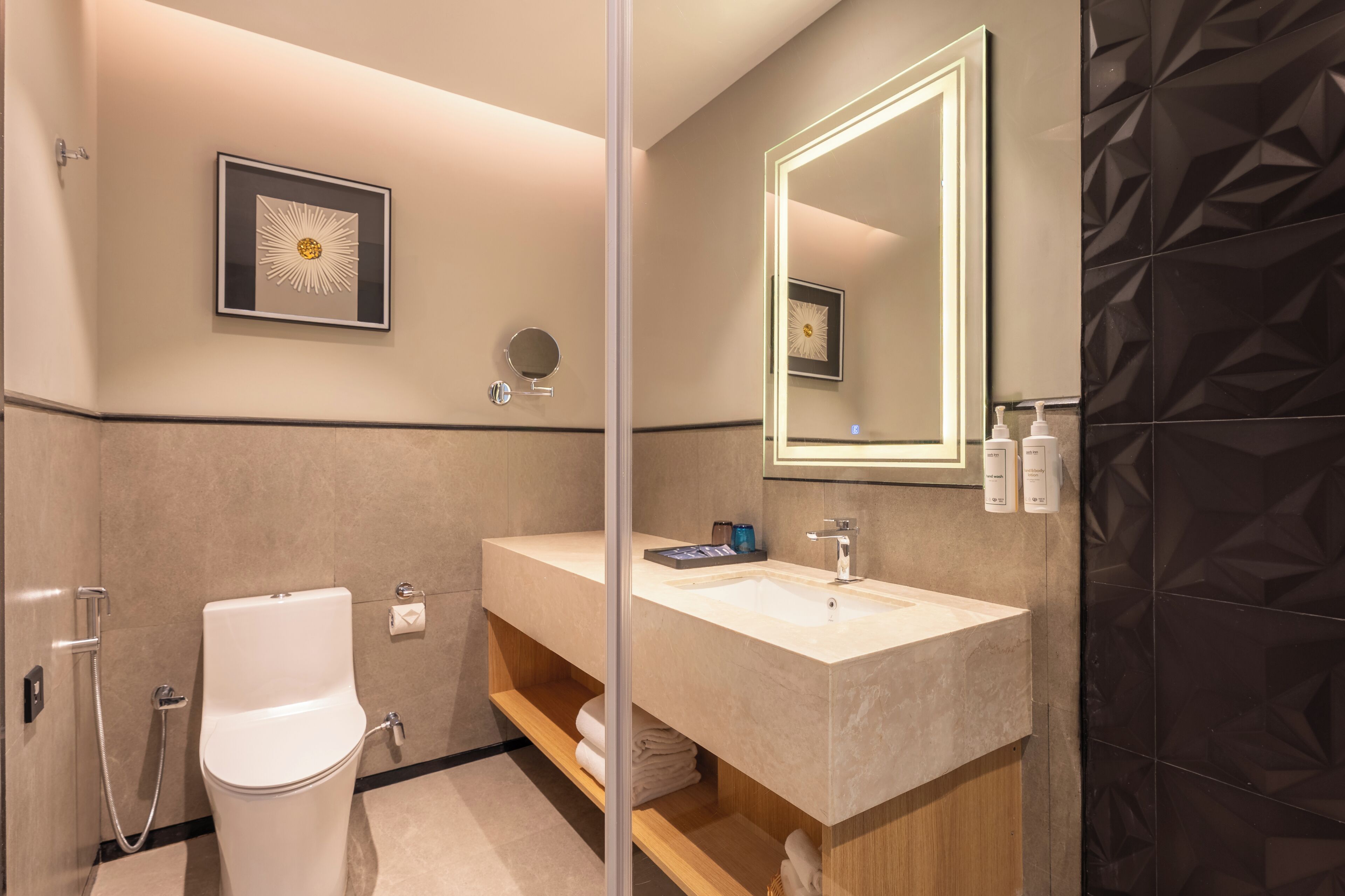 A modern bathroom with a toilet, sink, and shower. There is a mirror above the sink and a framed picture on the wall.
