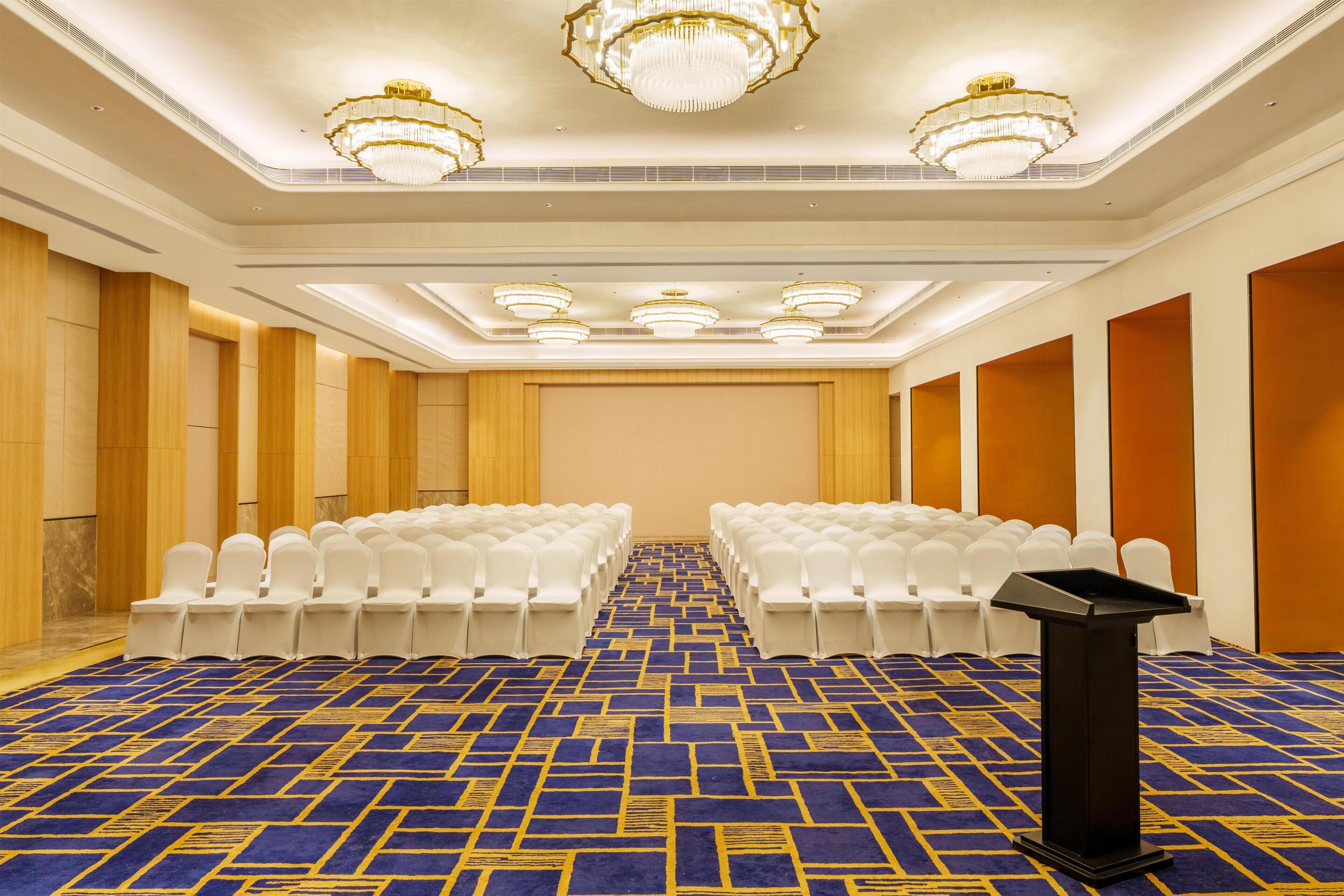 A conference room with rows of white chairs, a podium, and a patterned carpet.