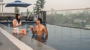 A couple in a swimming pool with a drink, a blue umbrella, and outdoor furniture in the background. - Park Inn By Radisson Jabalpur (Jabalpur)