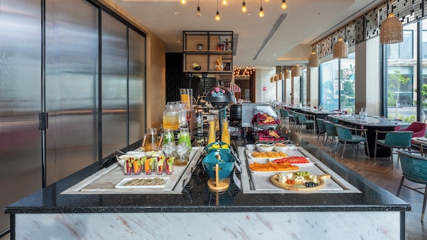 A breakfast buffet with various food items and beverages, a long counter with seating, and a modern interior design. - Park Inn By Radisson Jabalpur (Jabalpur)