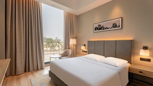 A hotel room with a large bed, two bedside lamps, a chair, a small table, and a window with curtains. - Park Inn By Radisson Jabalpur (Jabalpur)