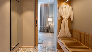A hotel hallway with a wooden bench, a robe hanging on the wall, and a view into a room with a chair and a lamp. - Park Inn By Radisson Jabalpur (Jabalpur)