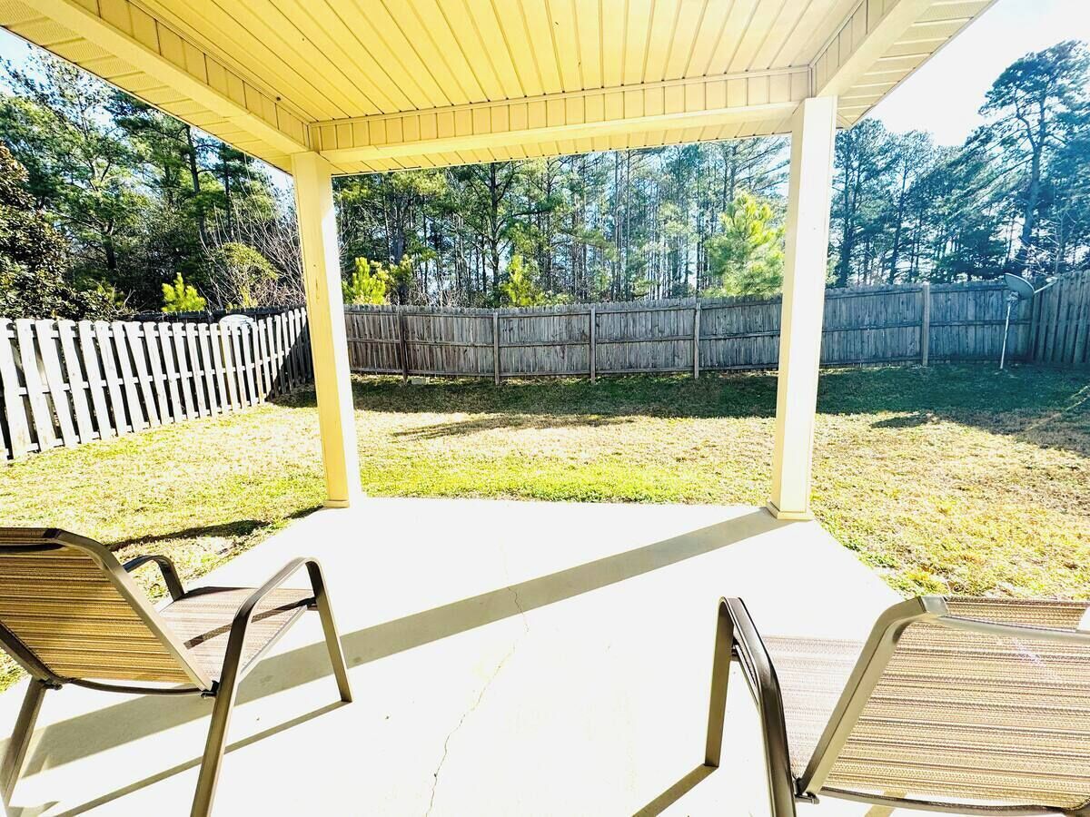 A covered patio with two chairs, a wooden fence, and a grassy yard.