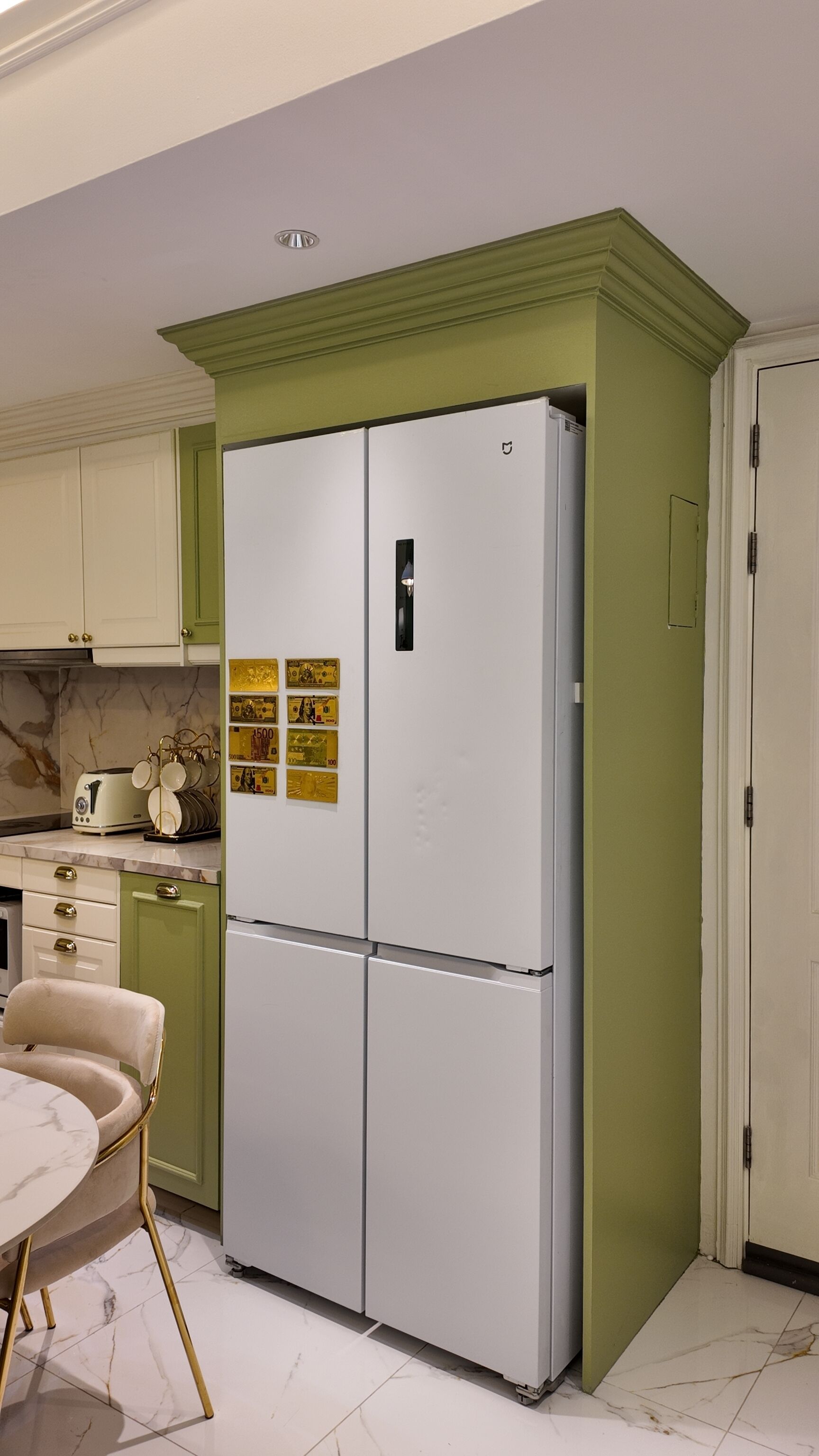 A kitchen with a white refrigerator, green cabinets, a marble countertop, a vintage toaster, and a gold-framed chair.