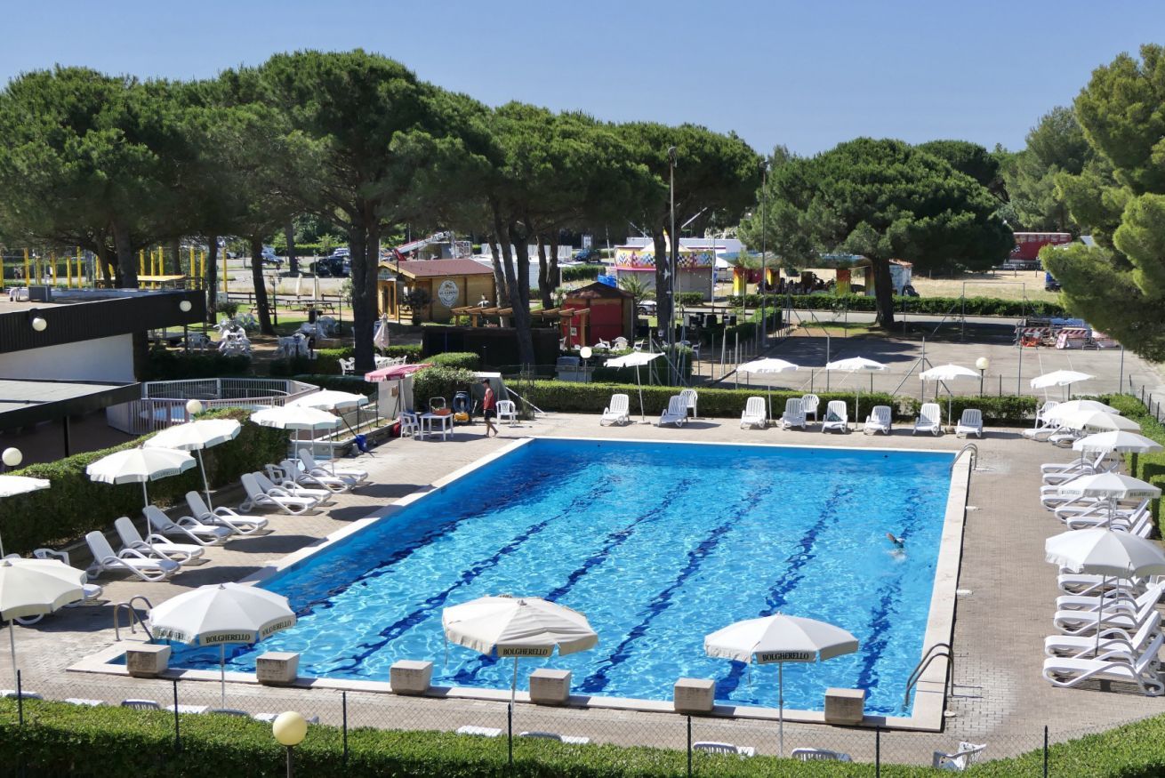 A swimming pool with lounge chairs and umbrellas, surrounded by trees and buildings.