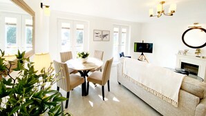 A bright, well-lit room with a dining table, chairs, a sofa, a TV on a tripod, and a fireplace. - The Degas Sea View Suite (Torquay)