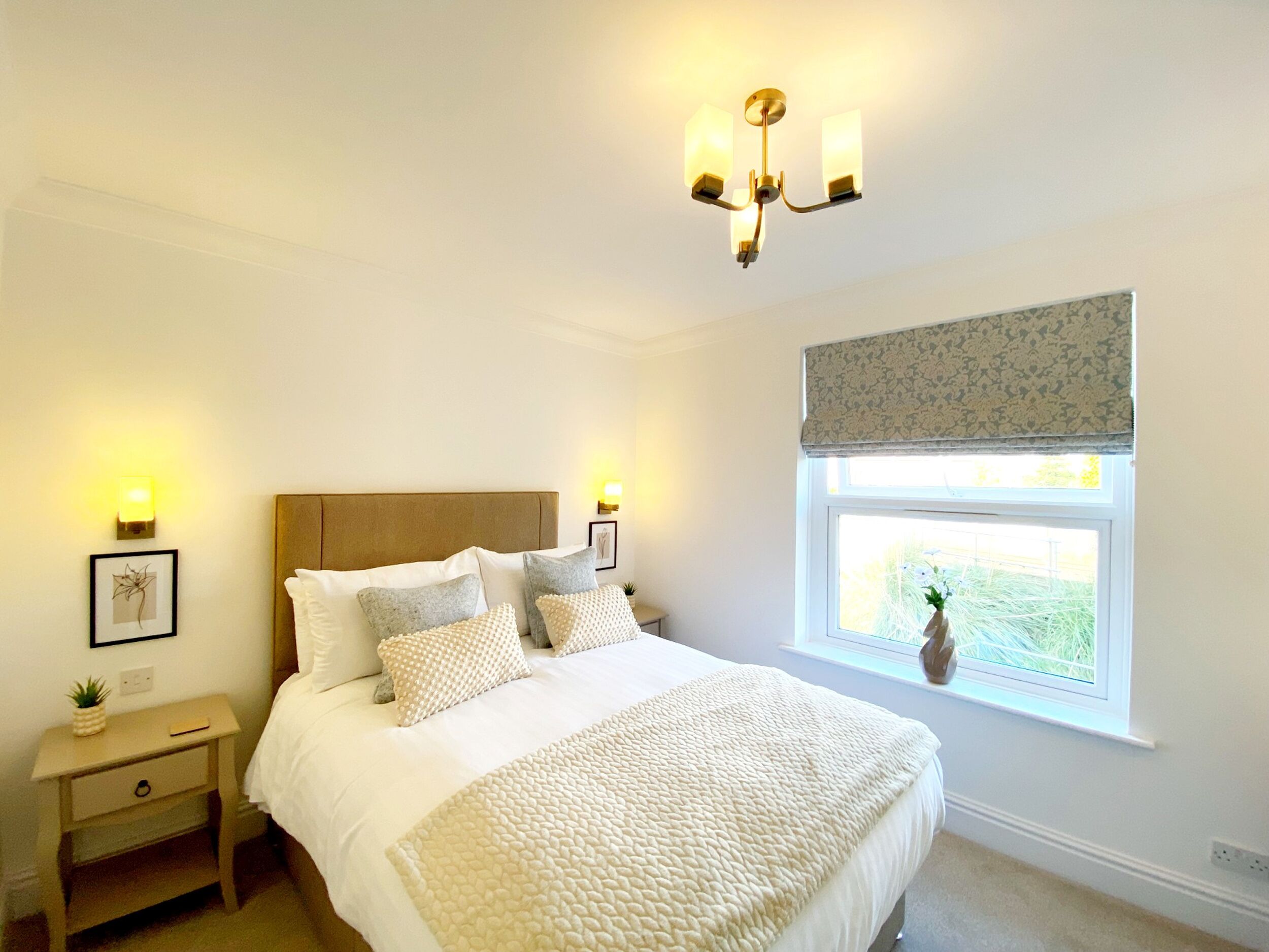 A bedroom with a large bed, a nightstand, a window with a view, and a chandelier.