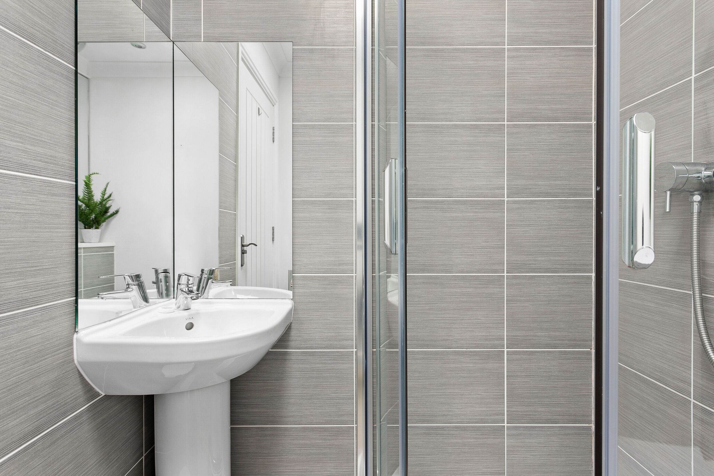 Ein modernes Badezimmer mit einer Duschkabine aus Glas, einem weißen Waschbecken und einem Spiegel.