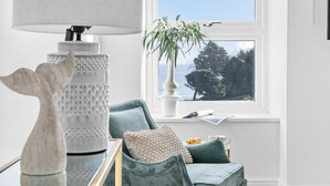 A room with a view of the sea, a lamp, a plant, and a sofa with cushions. - The Renoir Sea View Suite (Torquay)
