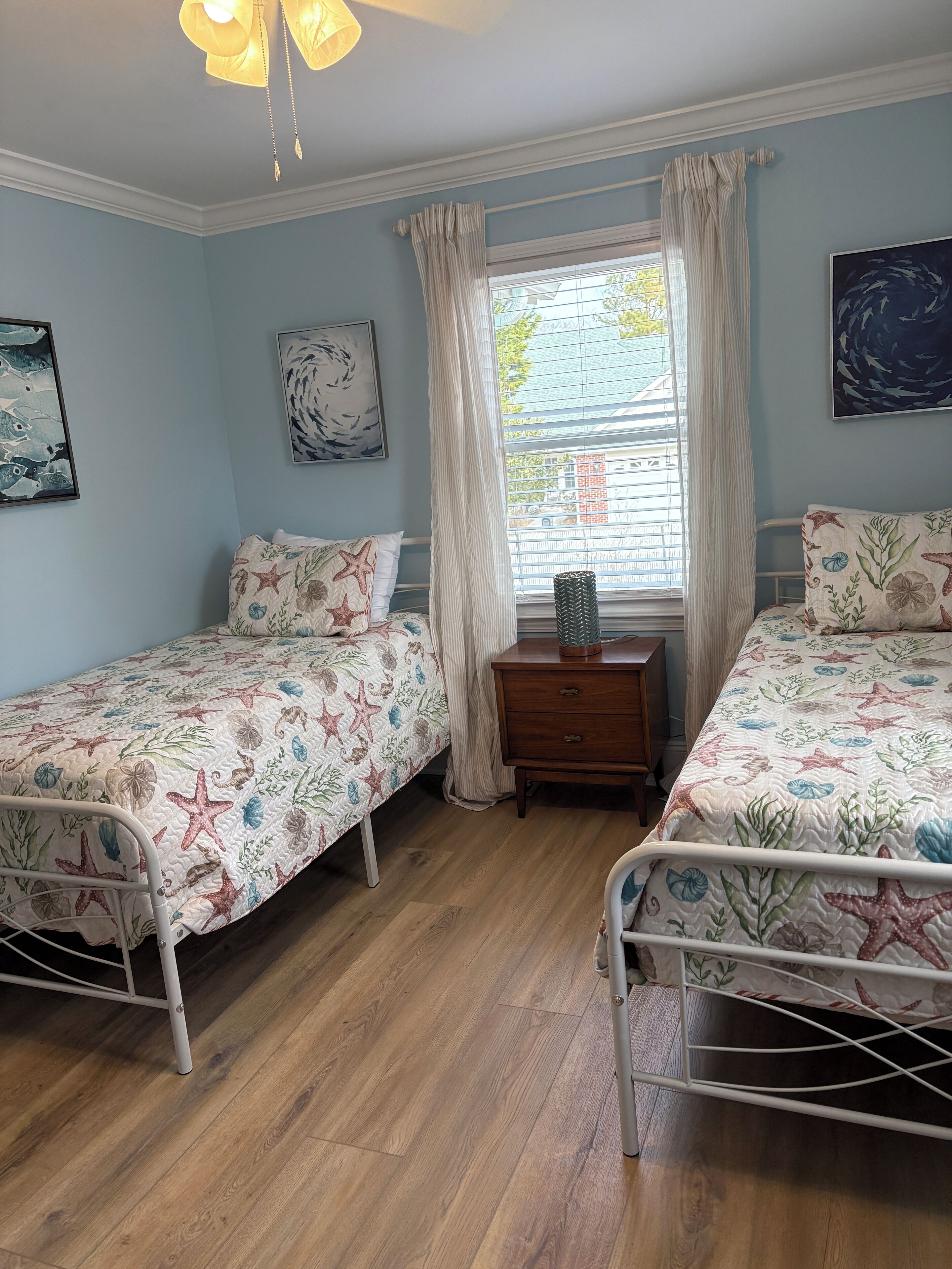 A bedroom with two single beds, a wooden dresser, and a window with curtains.