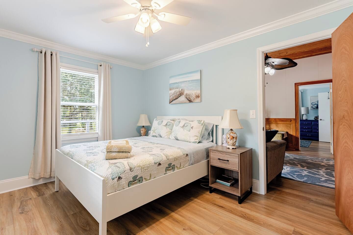 A bedroom with a bed, bedside tables, a ceiling fan, and a window with curtains.