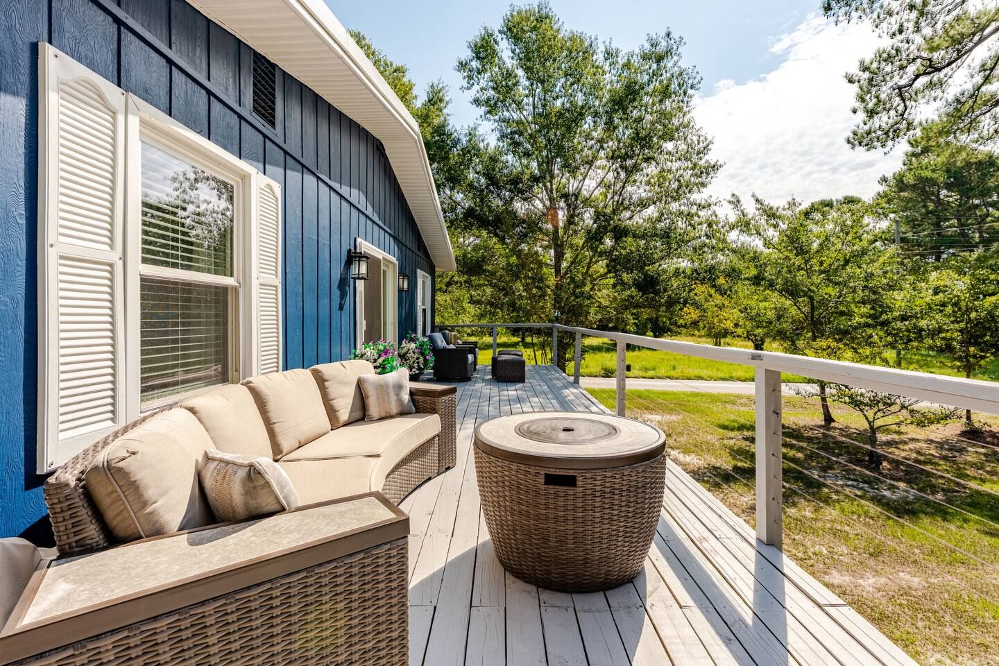 Une terrasse couverte, dotée d’un canapé et d’une table ronde, qui donne sur un espace verdoyant agrémenté d’arbres.