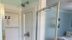 Ein Zimmer mit Dusche, einem Bett mit floralem Bettzeug und einer Tür mit Milchglasfenstern.