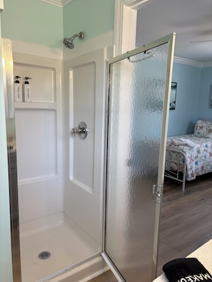 Une chambre avec une douche, un lit avec une literie à motifs floraux et une porte en verre dépoli.