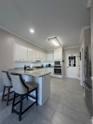 A modern kitchen with white cabinets, a granite countertop, and a built-in island with bar stools. - Abbeys at  WestLake , Wonderful 3-bedroom house with AC in charming Martinez. (Martinez)