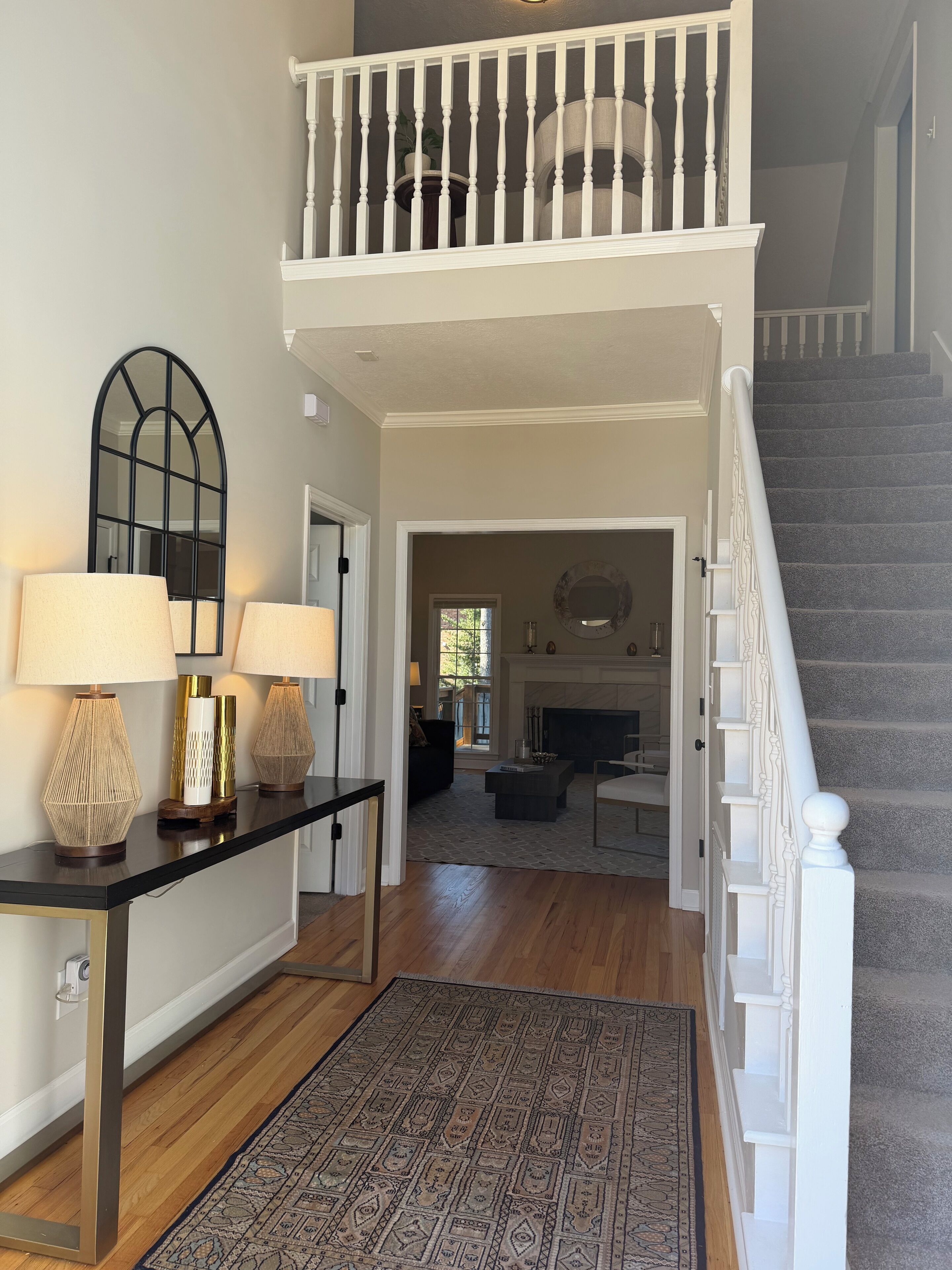 A spacious living area with a staircase, a console table with lamps, a patterned rug, and a view into the dining area.